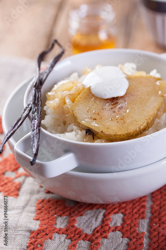 Rice with milk, cinnamon, honey, pear and yoghurt with in a white bowl.