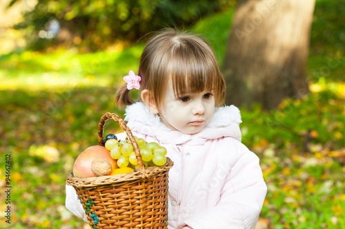     Cute little girl holding a basket full of fruit 