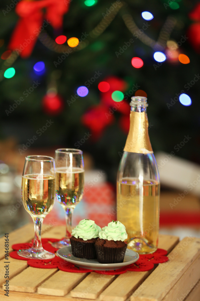Delicious cupcakes and champagne on table, on Christmas tree background Delicious cupcakes and champagne on table, on Christmas tree background