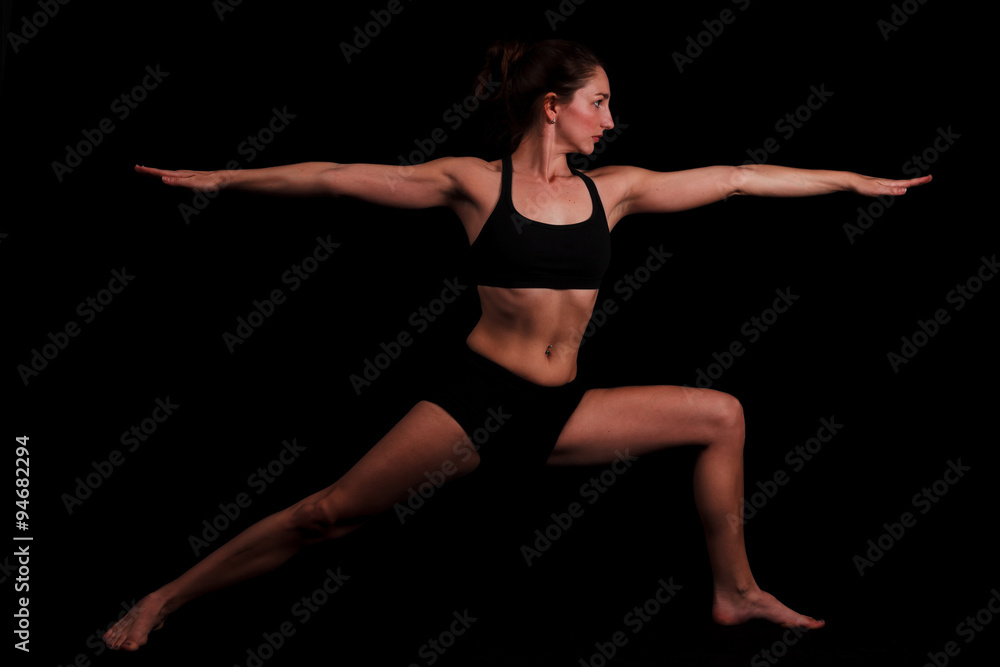 Woman practicing Warrior yoga pose on a black background