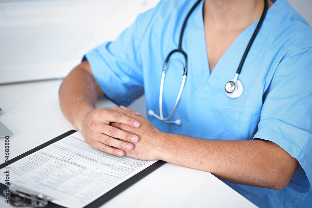 Portrait of unknown male surgeon doctor sitting at the table in hospital office, stethoscope Portrait of unknown male surgeon doctor sitting at the table in hospital office, stethoscope