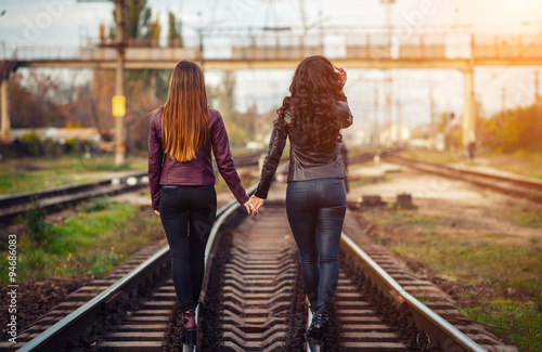 Foto two beautiful girls in leather jackets and tight pants go hand in hand rail at s