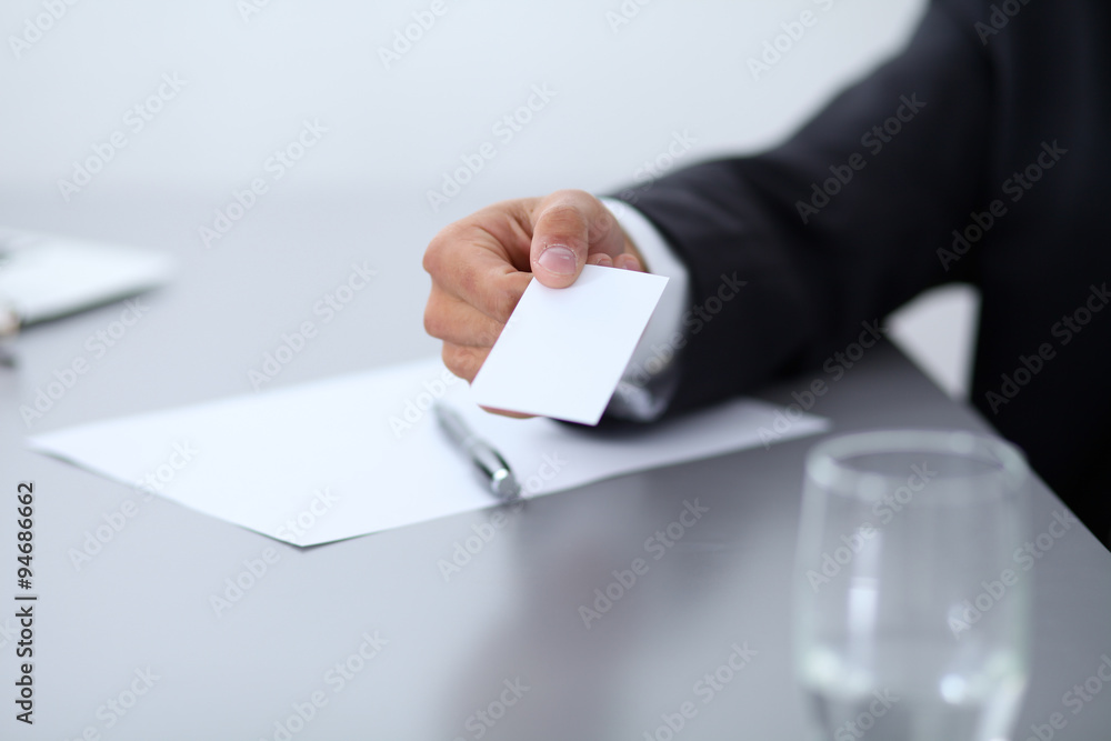 Close-up of businessman giving a business card, sitting at the table Close-up of businessman giving a business card, sitting at the table