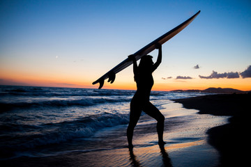 Young female surfer on beach in sunset