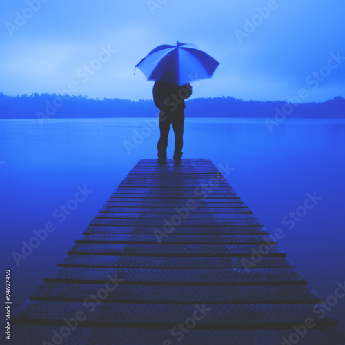 Man Holding an Umbrella on a Jetty by Tranquil Lake Concept