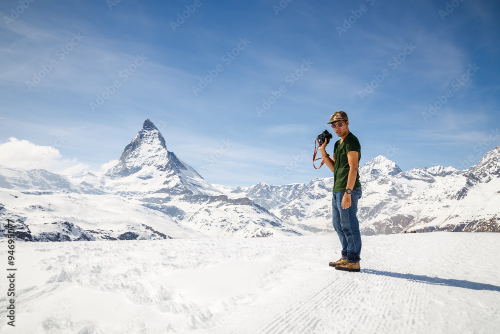 A man standing on the snow holding camera with the background of