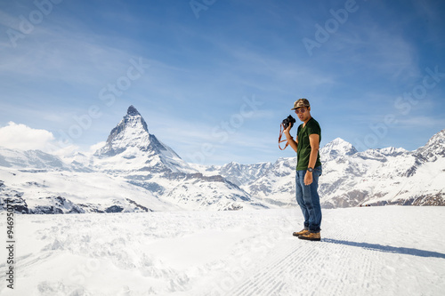 A man standing on the snow holding camera with the background of