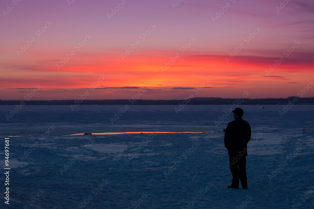 man watching the sunset on the winter lake