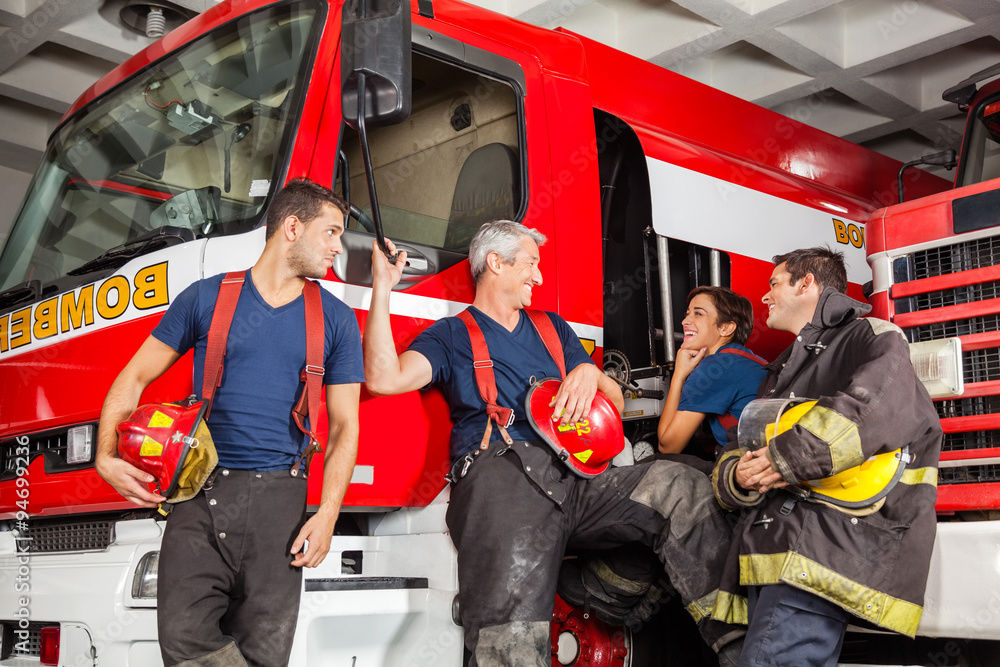 Fototapeta premium Happy Firefighters Conversing While Leaning On Trucks