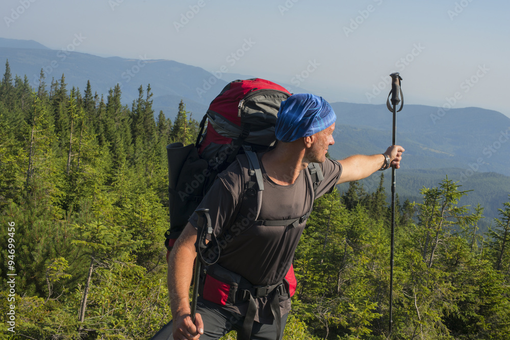 Hiker man standing on the mountain top in sunny day and shows at