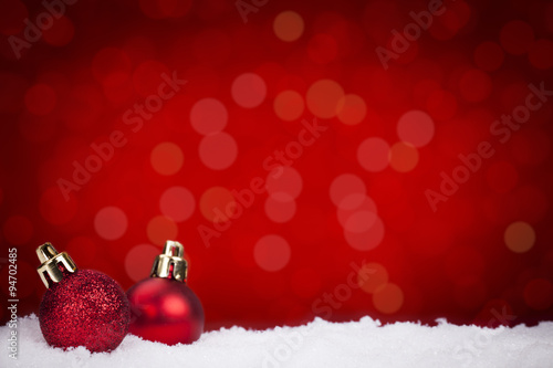 Red Christmas baubles on snow with a red background