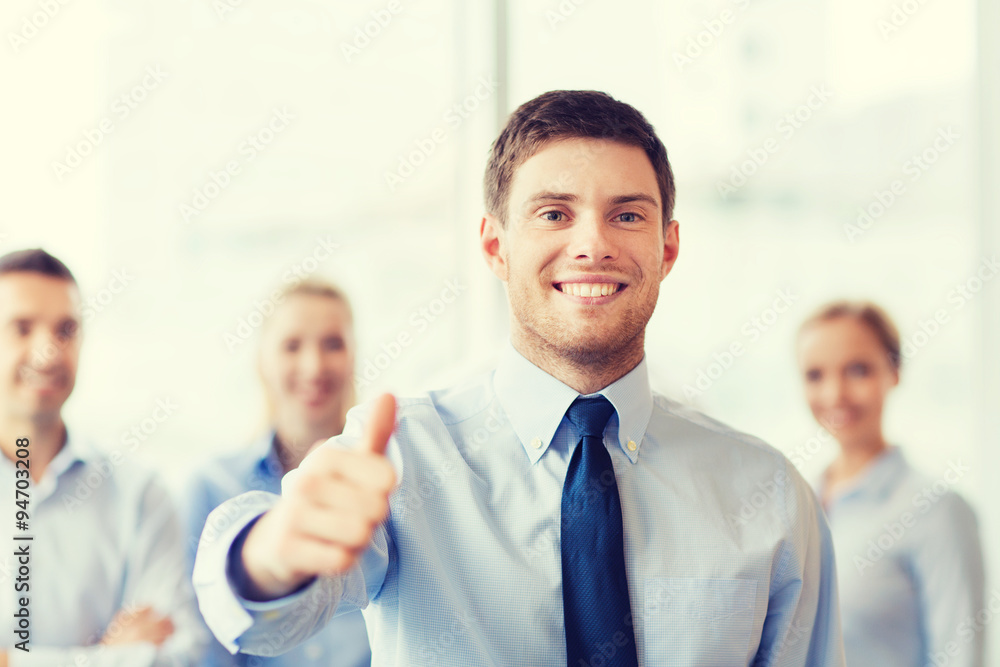 smiling businessman showing thumbs up in office smiling businessman showing thumbs up in office