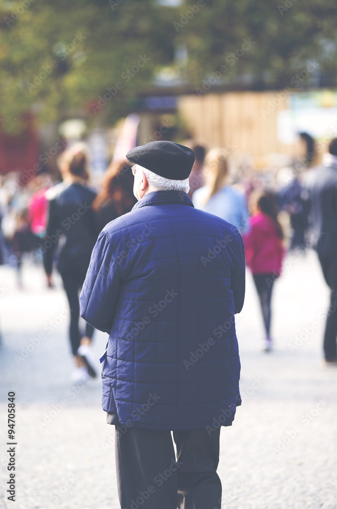 An elderly man is standing in the city. Some unidentified person are walking in the streets. Image has a vintage effect applied. An elderly man is standing in the city. Some unidentified person are walking in the streets. Image has a vintage effect applied.