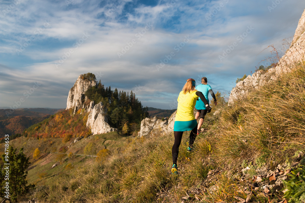 two woman running up the hill on the rocky trail in the autumn nature