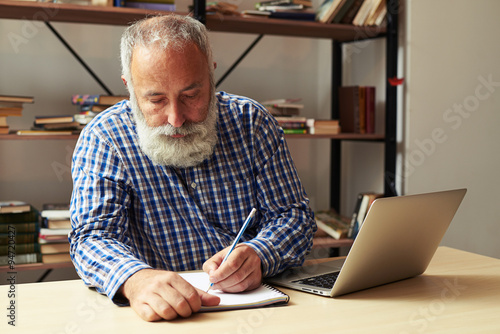 senior man writing in notepad at his working place