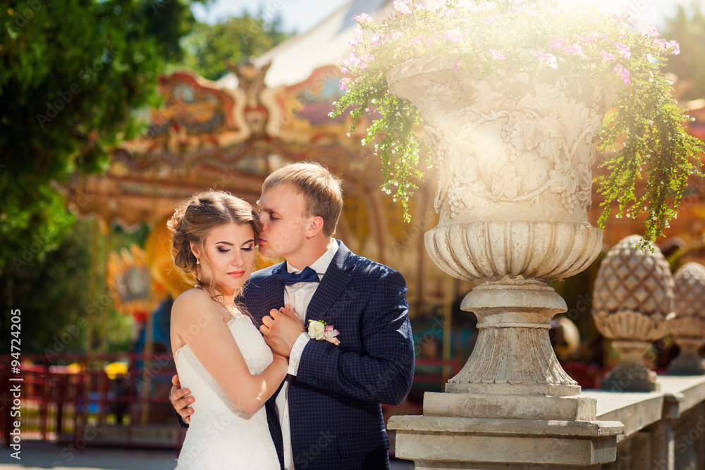 Groom kissing bride in front of carousel in park