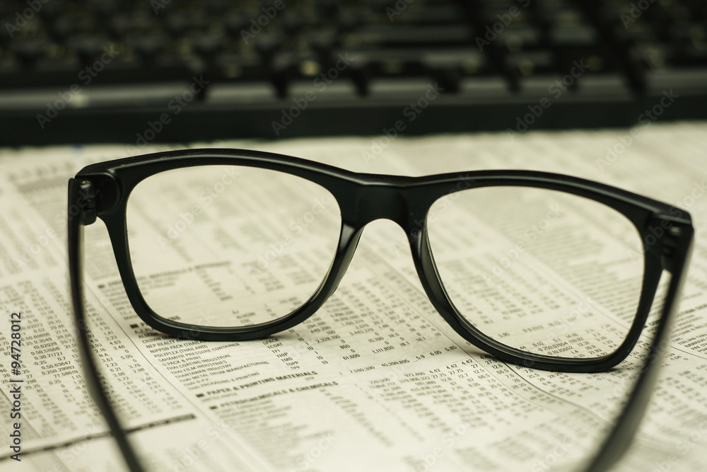 keyboard and a black eyeglasses on a financial newspaper keyboard and a black eyeglasses on a financial newspaper