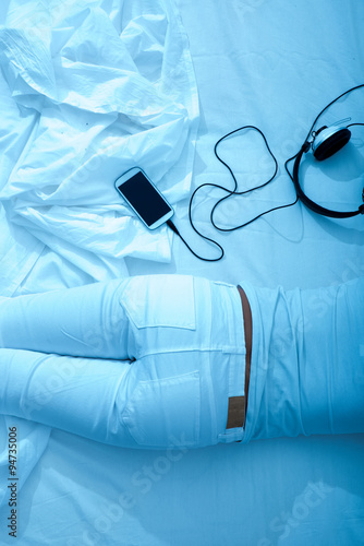 Woman laying in the bed with headphones and a smartphone.