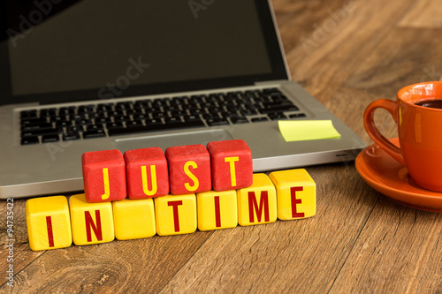 Just In Time written on a wooden cube in front of a laptop