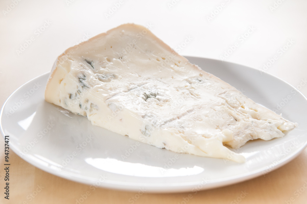 Big slice of fresh Gorgonzola cheese on white ceramic dish