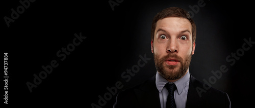 Closeup portrait of happy young handsome businessman looking shocked surprised in full disbelief open mouth eyes, on black background. Positive human emotion facial expression feeling reaction.