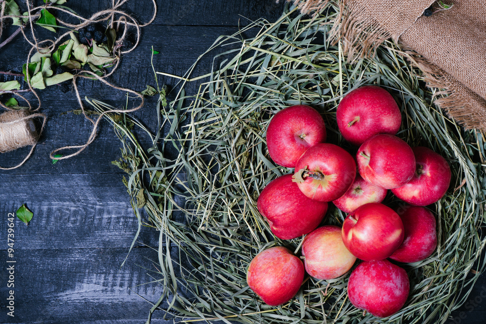 Red apples on green grass and textiles on a black wooden background top view