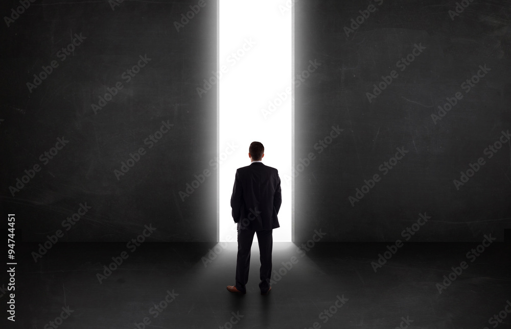Business person looking at wall with light tunnel opening Business person looking at wall with light tunnel opening