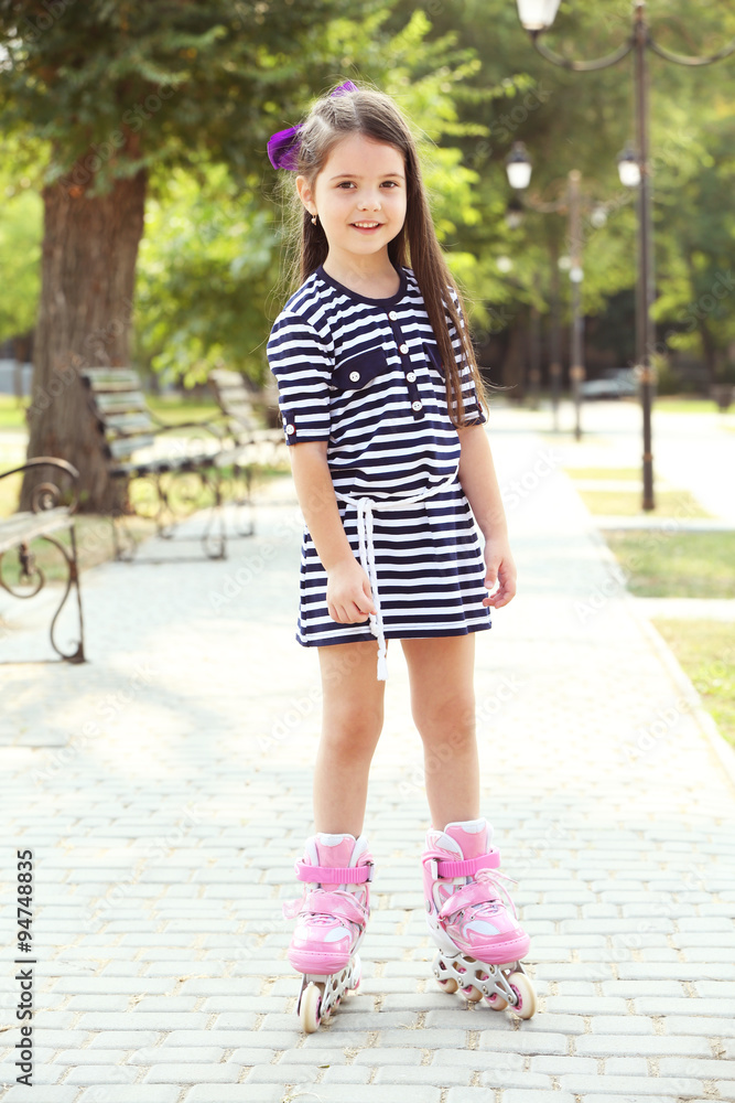 Happy little girl in striped dress with roller skates outdoors Happy little girl in striped dress with roller skates outdoors