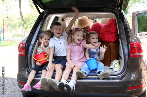 Three beautiful girls and boy sit on a car trunk and laughing © Africa Studio