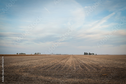View of an empty corn field after harvest, under a sunset sky.