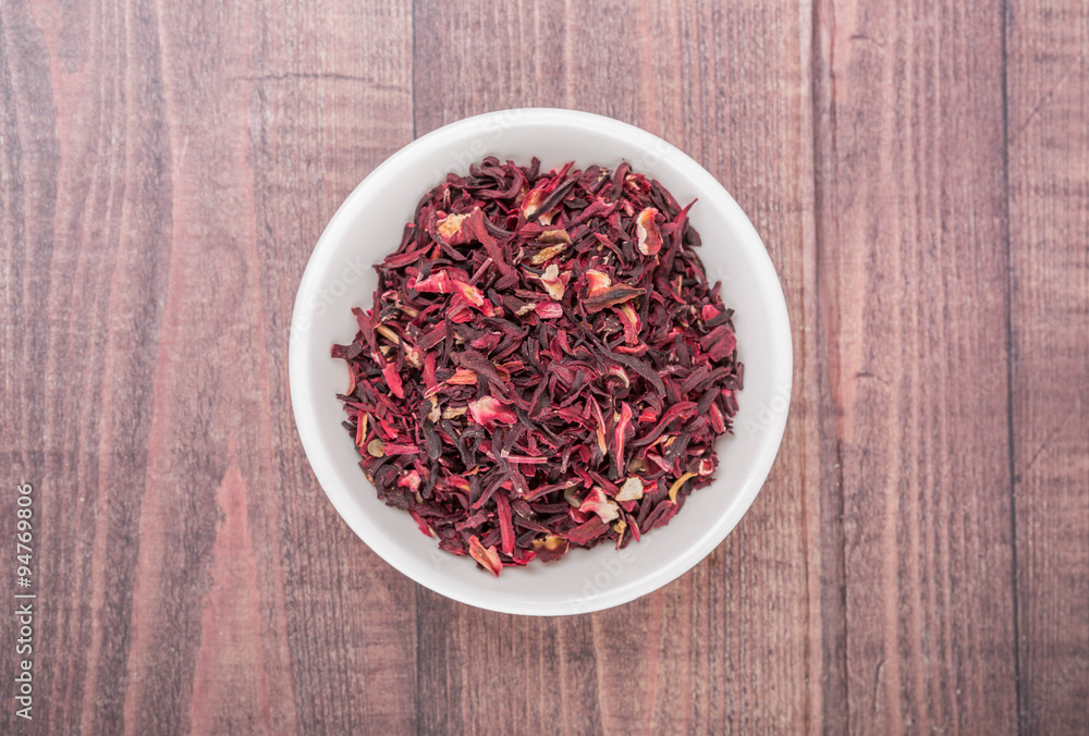 Dried red hibiscus tea leaves in white bowl over wooden background