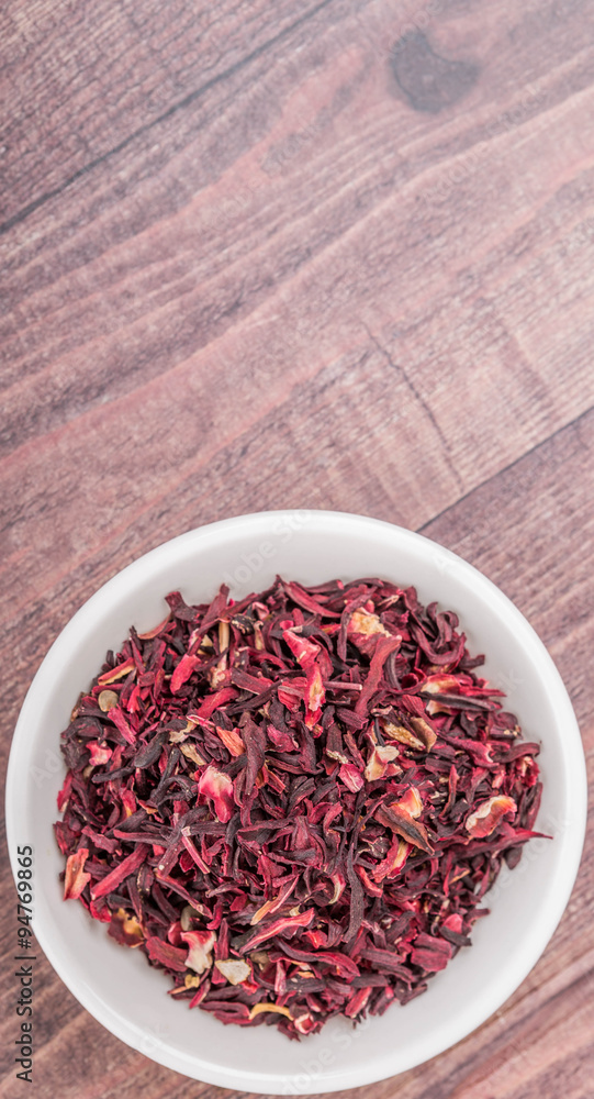 Dried red hibiscus tea leaves in white bowl over wooden background Dried red hibiscus tea leaves in white bowl over wooden background