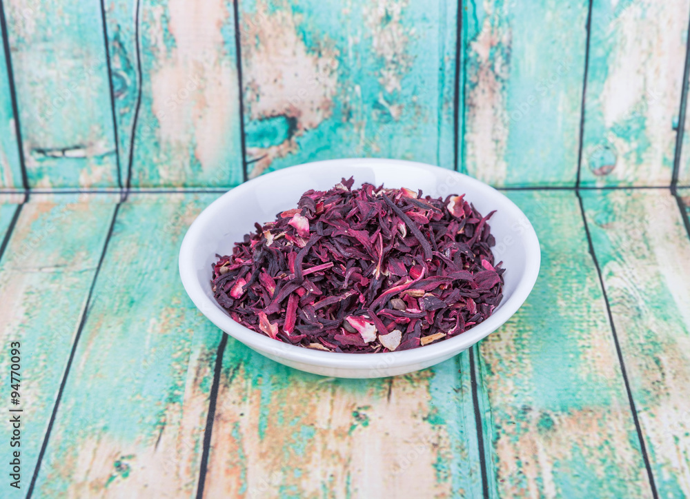 Dried red hibiscus tea leaves in white bowl over wooden background Dried red hibiscus tea leaves in white bowl over wooden background