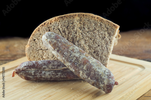 Pane nero e salamino, salame affettato su tagliere con pane scuro, coltello per salumi photo