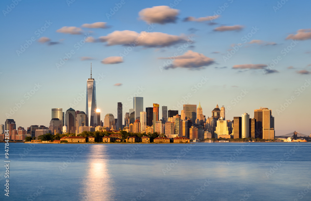 Skyline of New York City, Lower Manhattan. Ellis Island appears in front of the Financial District’s skyscrapers at sunset. View from Liberty State Park across New York Harbor.