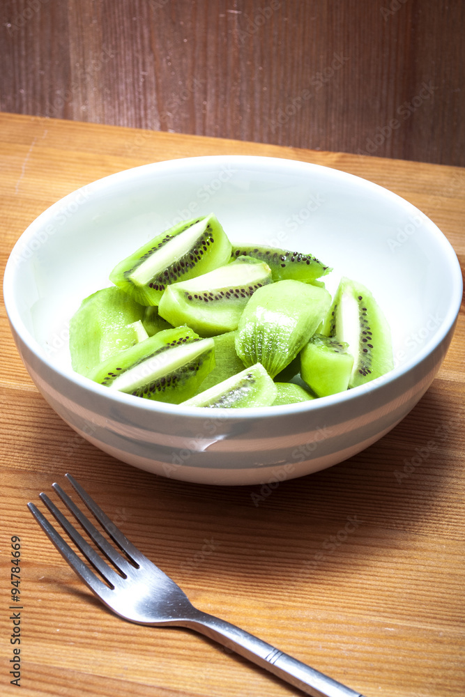 Bowl of delicious chopped kiwi only salad in a rustic kitchen , on a wooden table with a metal fork in the frame Bowl of delicious chopped kiwi only salad in a rustic kitchen , on a wooden table with a metal fork in the frame