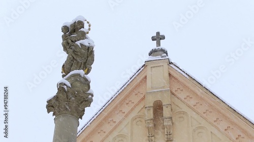 Statue of Virgin Mary and Jesus in the background church in the winter and snowing
