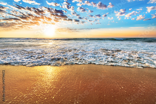 Fototapeta Naklejka Na Ścianę i Meble -  Colorful ocean beach sunrise with deep blue sky and sun rays.