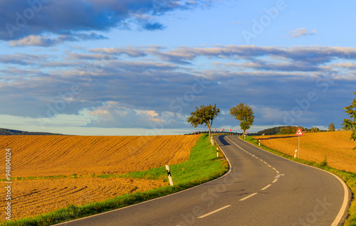 Panoramic landscape of colorful yellow-green hills with ground road, blue sky and clouds 