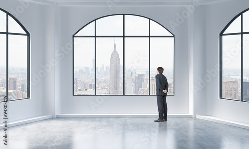 Rear view of a person in formal suit who is looking out the window in a modern loft interior. New York city view.