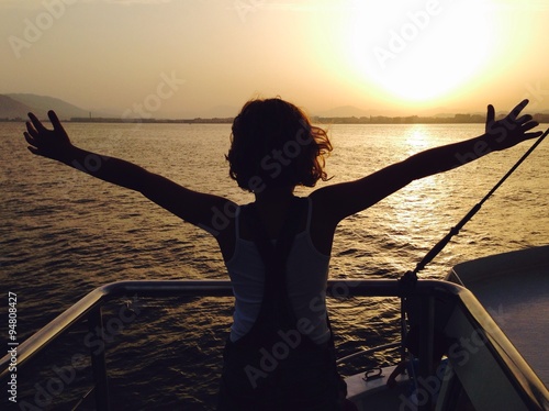 Obraz na płótnie niña en la proa de un barco con los brazos abiertos en el ocaso del dia