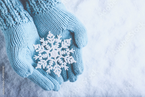 Fototapeta Naklejka Na Ścianę i Meble -  Female hands in light teal knitted mittens with sparkling wonderful snowflake on snow background. Winter and Christmas concept
