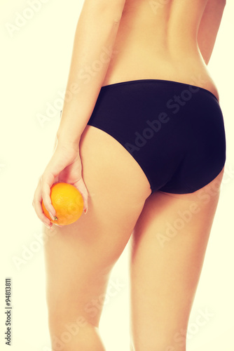 Woman holding orange next to buttocks.