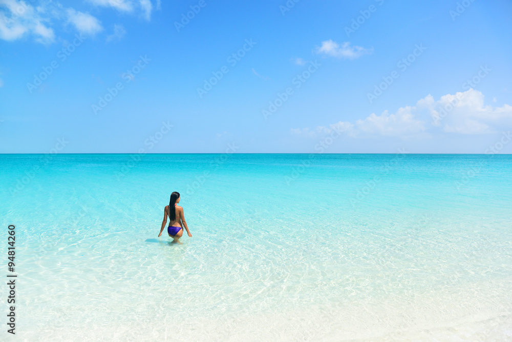 Beach holiday person swimming in blue ocean. Sexy bikini woman relaxing enjoying her tropical vacation in the Caribbean in a paradise destination with perfect turquoise water and white sand.