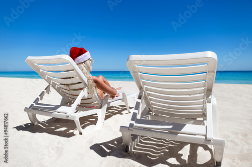 Woman in Santa Claus Hat sitting on sunbed at caribbean sandy be