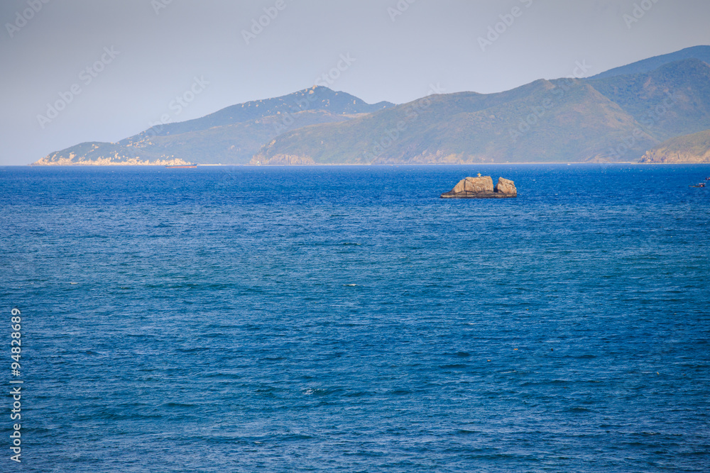 fishing boat amidst azure sea against hilly tropical island