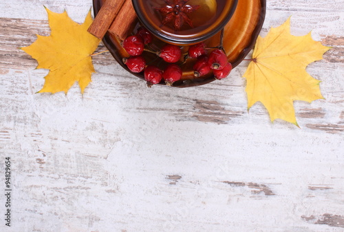 Cup of tea with lemon, spices and autumnal leaves on wooden background, copy space for text