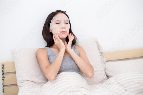 Woman using facial mask in bed