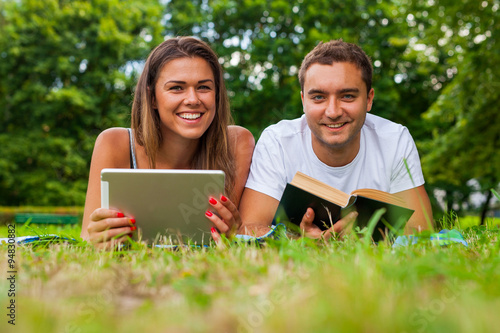 Couple lying on a grass with tablet and book
