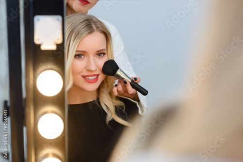 Model sitting in front of mirror while applying blush. photo